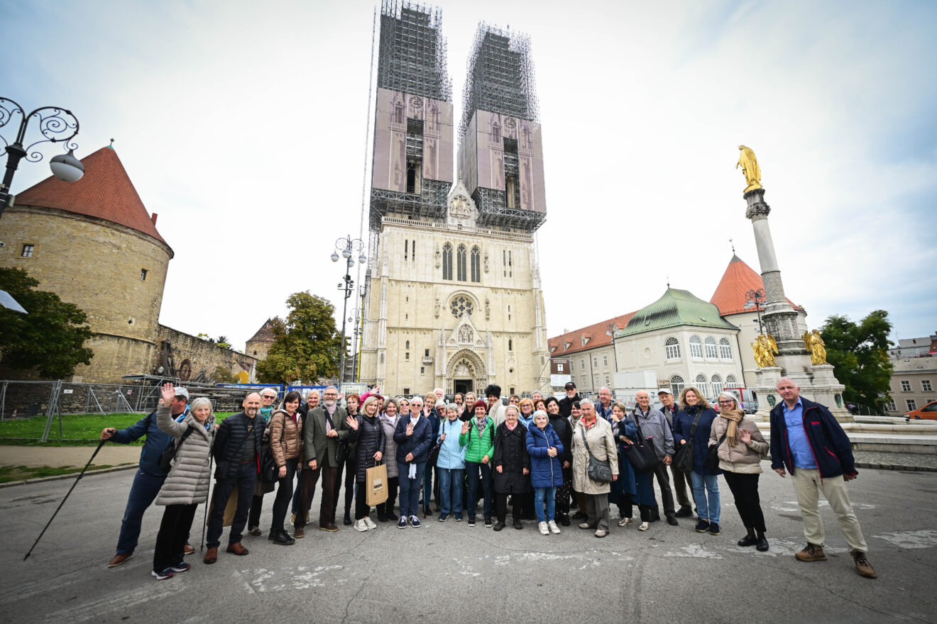 Velika skupina ljudi stoji pred zagrebško katedralo, ki je v gradbenih odrih, med izletom.